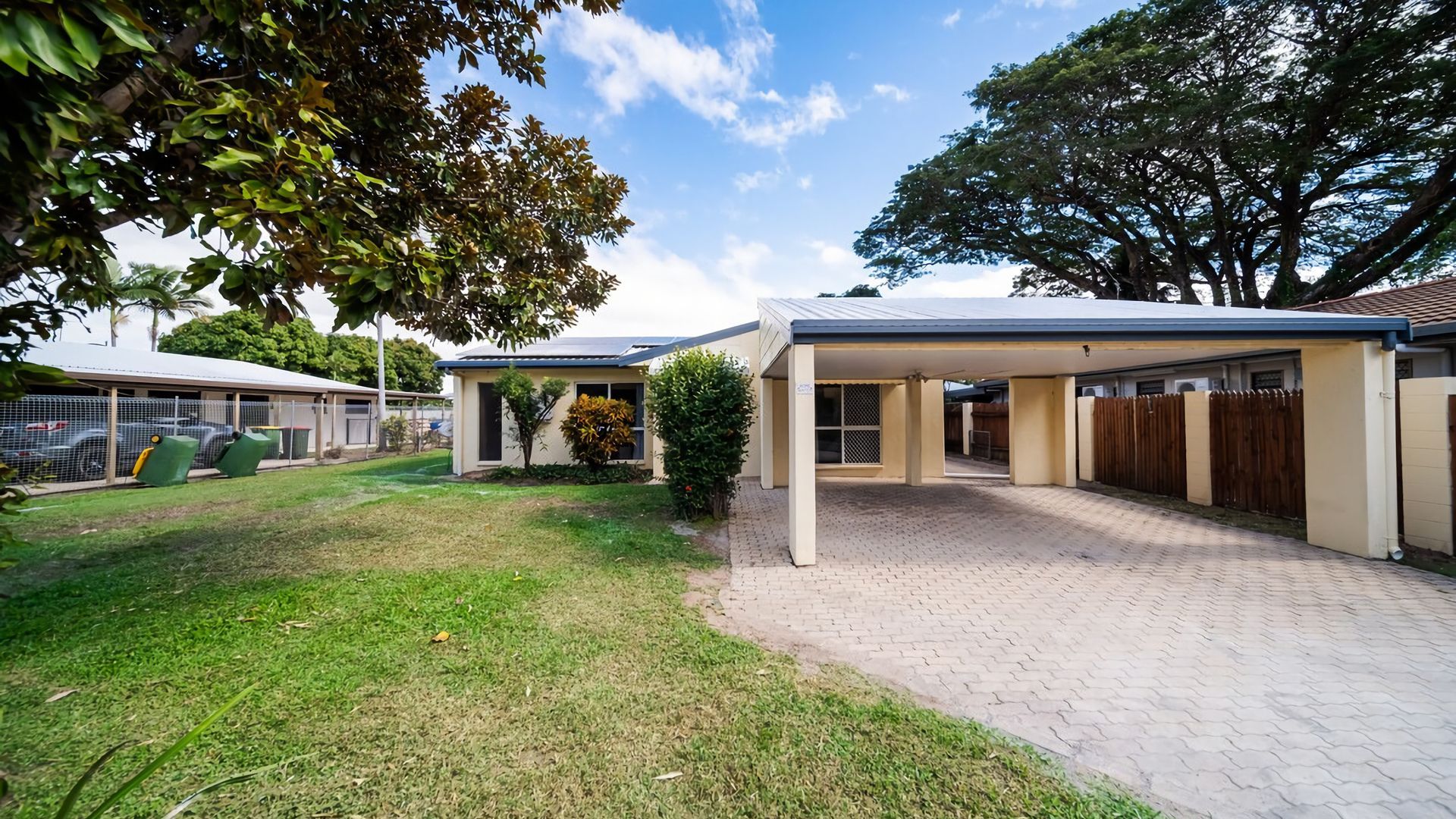 A residential property with a covered patio, a fenced yard, and a building with a flat roof.