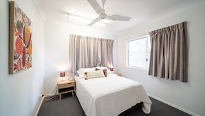 Een slaapkamer met een bed, nachtkastjes, een plafondventilator en een raam met gordijnen.