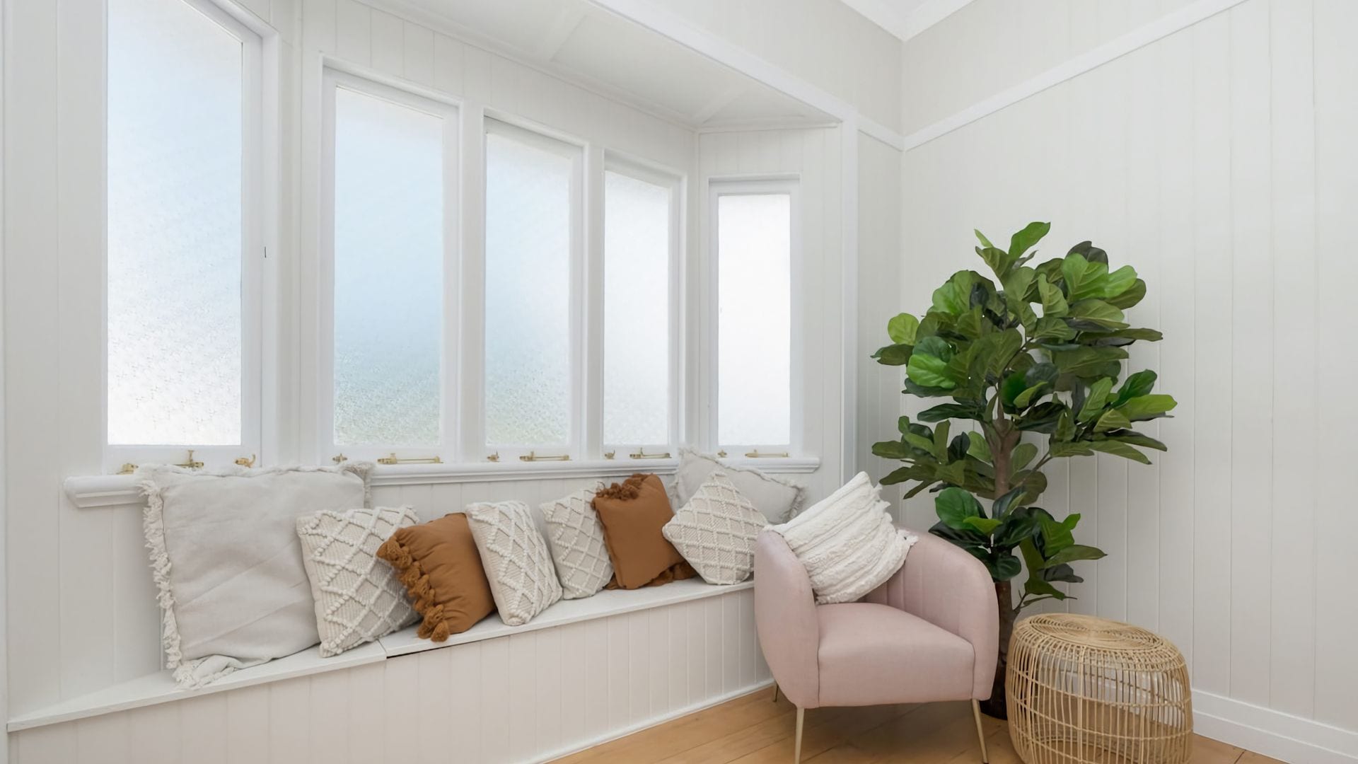 Ein Zimmer mit einer fest eingebauten Bank an einer weißen Wand, einem Blumentopf und einem Korbstuhl.