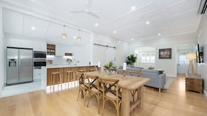 Une cuisine moderne dotée d’un réfrigérateur encastré, un coin repas avec une table et des chaises en bois, et un canapé gris dans un espace de vie lumineux.