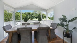 A covered patio with a wooden table and wicker chairs, surrounded by white railings and potted plants. - Grand 4BR Queenslander on Harold – Sleeps 7 (West End)