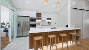 A modern kitchen with a central island, stainless steel appliances, and wooden bar stools. - Grand 4BR Queenslander on Harold – Sleeps 7 (West End)