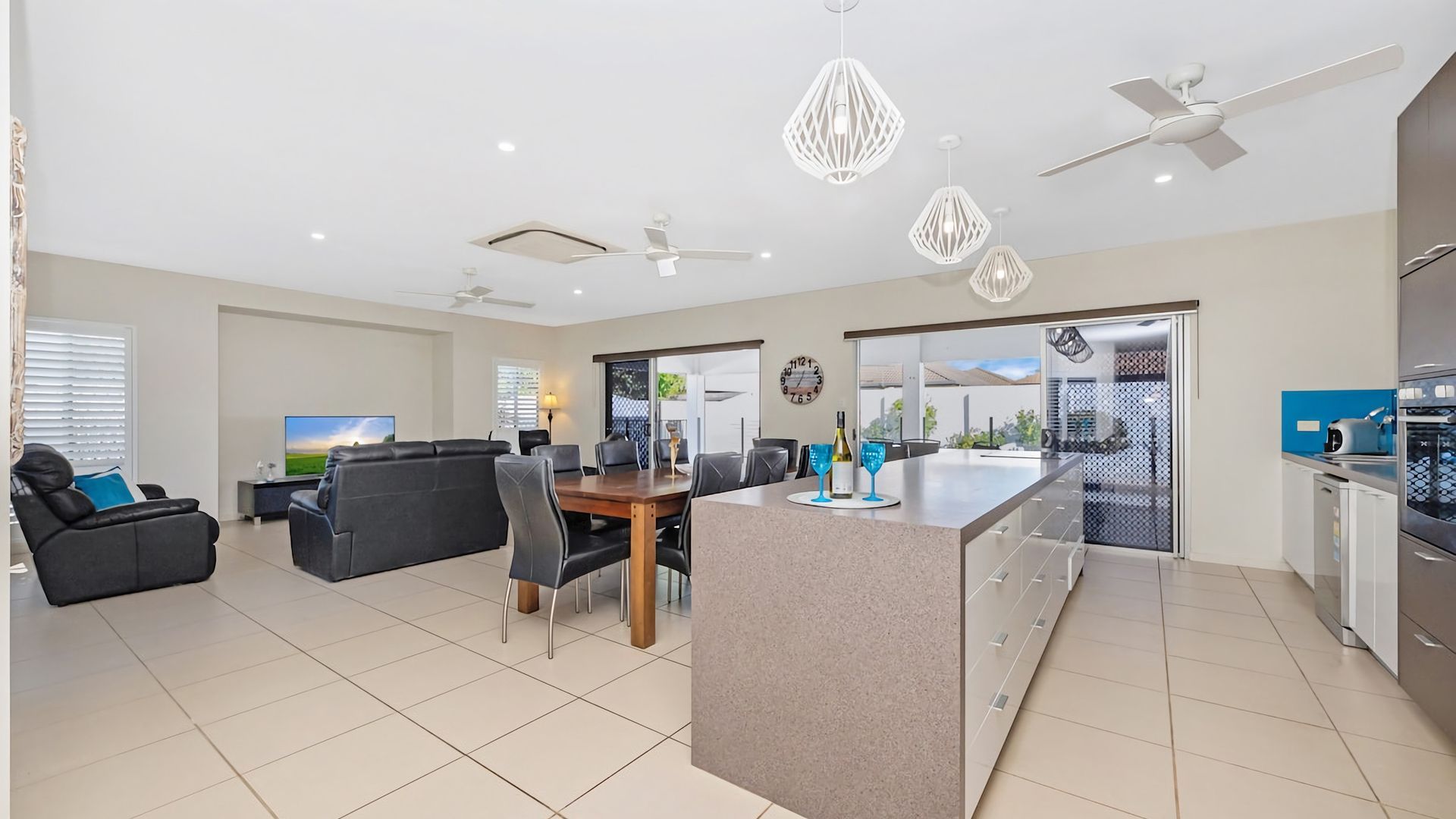 Cocina moderna con isla central, comedor con mesa y sillas, sala de estar con sofá y un ventilador de techo.