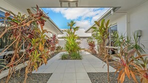 A pathway leading to a house with a covered patio area, surrounded by various plants and a clear sky. - Waterlily Oasis Stylish 4 Bedroom Stay (Douglas)