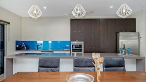A modern kitchen with a central island, dark cabinets, and a stainless steel refrigerator. - Waterlily Oasis Stylish 4 Bedroom Stay (Douglas)