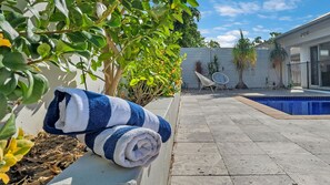 Ein Poolbereich mit gefliestem Boden, einem weißen Zaun und einem blau-weißen Handtuch auf einer Ablage.
