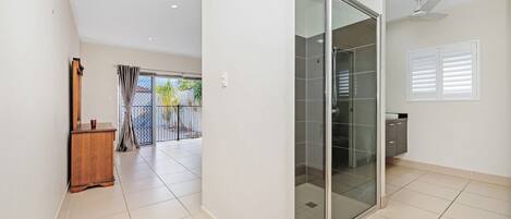 A modern bathroom with a glass shower enclosure, a ceiling fan, and a view of the outdoor balcony.