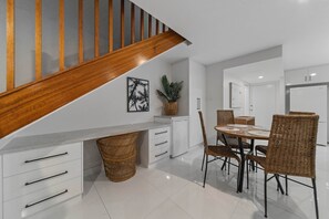 Una cocina moderna con armarios blancos, una escalera de madera y un comedor con sillas de mimbre.