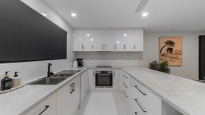 Una cocina moderna con armarios blancos, electrodomésticos de acero inoxidable y una pizarra en la pared izquierda.
