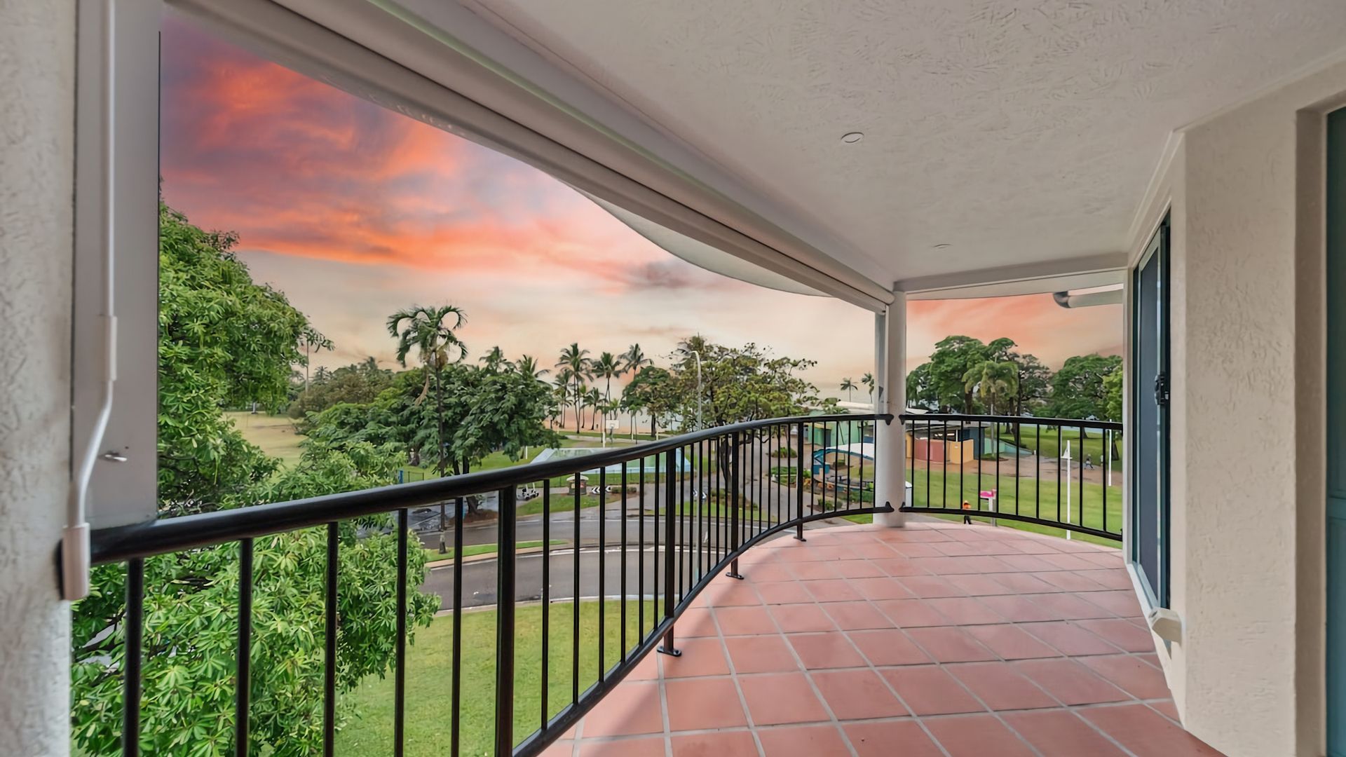 A balcony with a view of a park and a sunset.