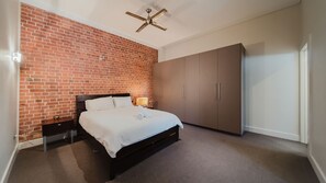 A bedroom with a brick wall, a bed, a wardrobe, and a ceiling fan. - Flinders Manhatten Residence (Townsville City)