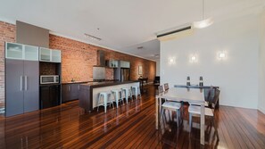 A modern kitchen with a brick wall, wooden flooring, and a dining area with a table and chairs. - Flinders Manhatten Residence (Townsville City)
