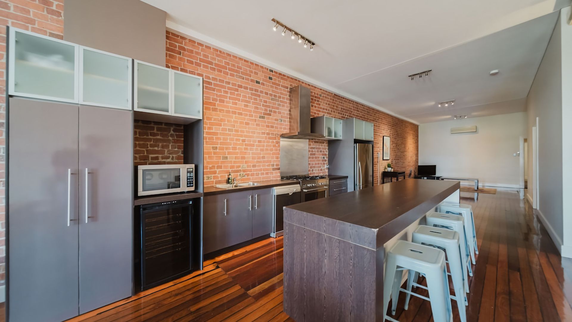 A modern kitchen with a brick wall, stainless steel appliances, and wooden flooring.