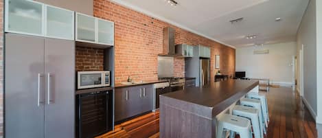 A modern kitchen with a brick wall, stainless steel appliances, and wooden flooring.