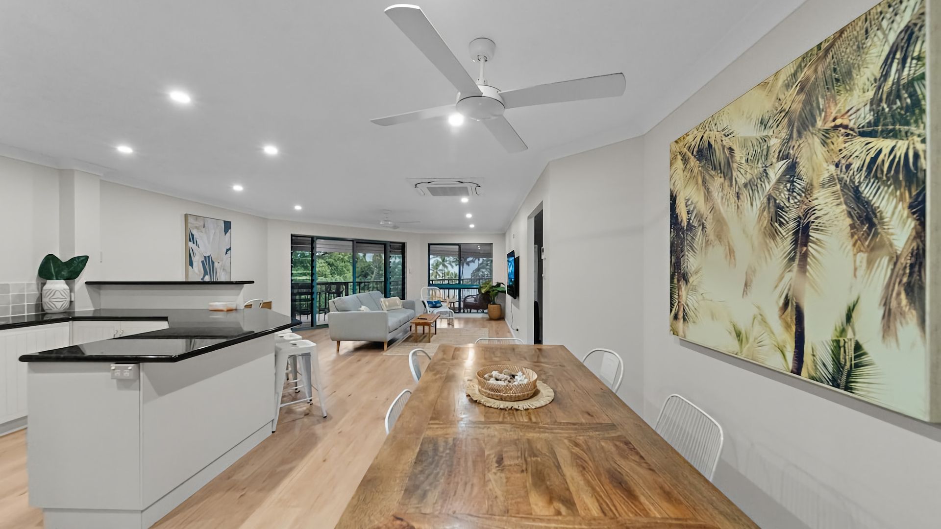 A modern kitchen with a dining area, large windows, and a ceiling fan.