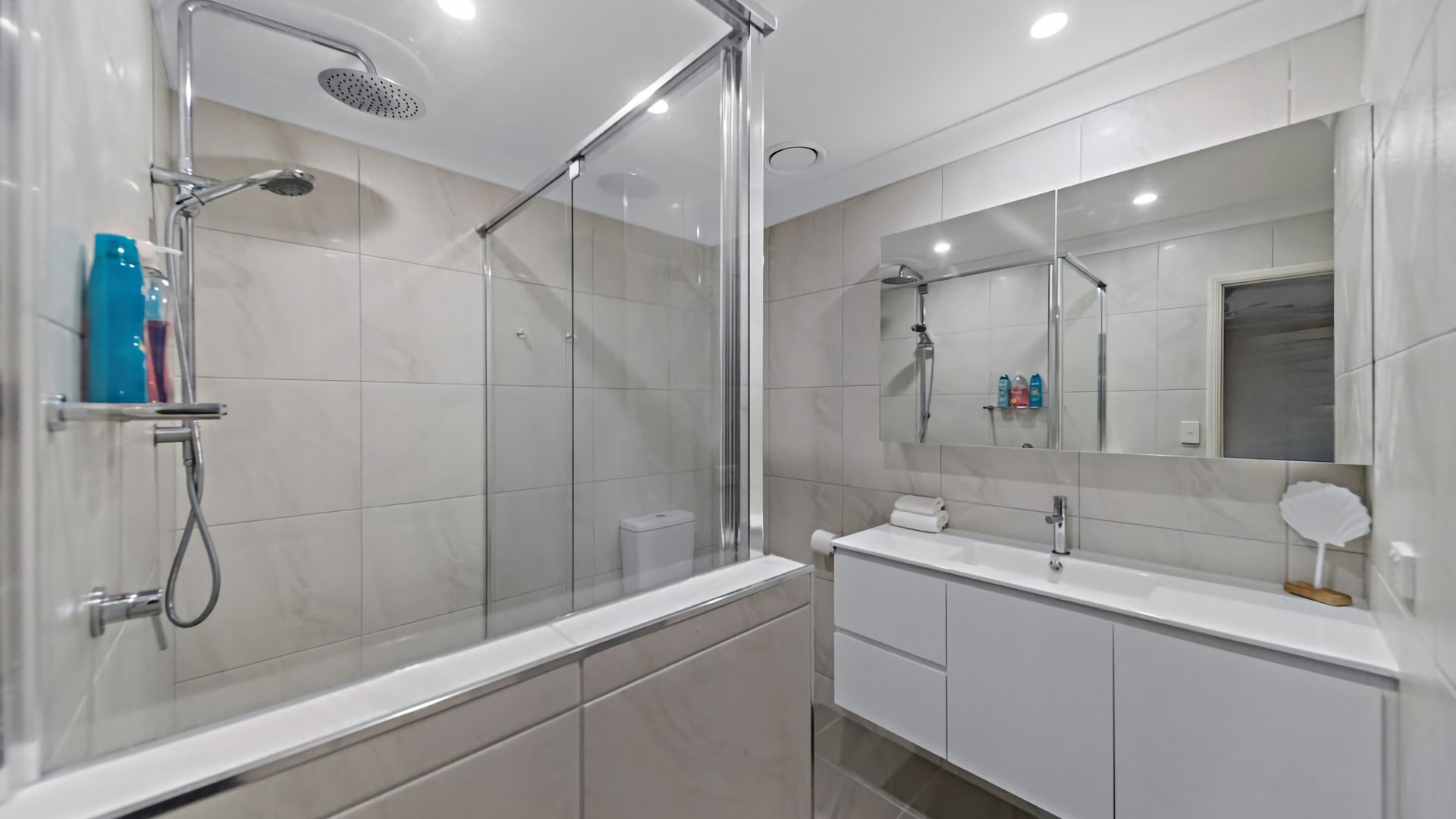 A modern bathroom with a glass-enclosed shower, a white vanity with a mirror, and a toilet.