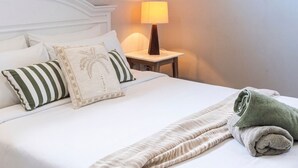 Ein ordentlich bezogenes Bett mit Kissen, einer Lampe und einem zusammengerollten Handtuch auf einer weißen Bettdecke.