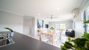 A modern kitchen with a central island, dining area with white chairs, and a living space with a sofa and a TV.