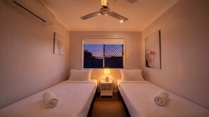 Ein Hotelzimmer mit zwei Betten, einem Deckenventilator, einem Fenster mit Blick und Kunstwerken an den Wänden.