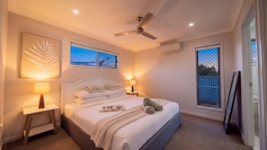A hotel room with a bed, bedside lamps, a ceiling fan, and two windows with a view. - The Northside Haven (Burdell)