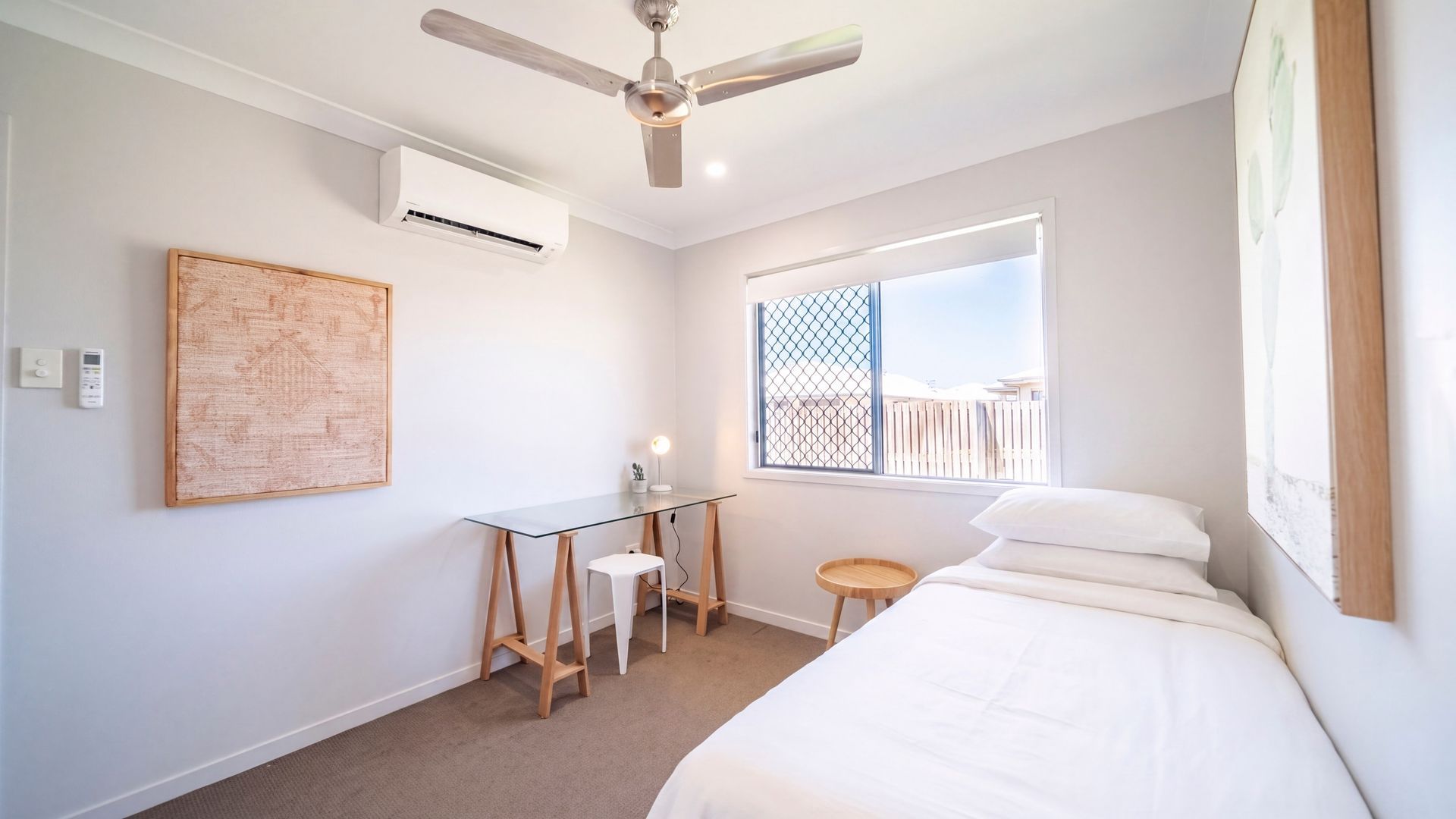 Ein Schlafzimmer mit Bett, Schreibtisch, Stuhl, Deckenventilator, Klimaanlage, Fenster mit Blick und einem Wandbild.