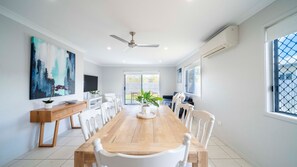 A modern dining room with a wooden table, white chairs, a ceiling fan, and a large window with a view.