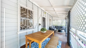 A covered porch with a wooden table and bench, a sofa, and a lattice screen. - Palm Grove Cottage and Private Studio (South Townsville)