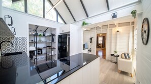 A modern kitchen with black countertops and white cabinetry, a dining area with a white sofa and a small table, and a large window providing natural light. - Palm Grove Cottage and Private Studio (South Townsville)