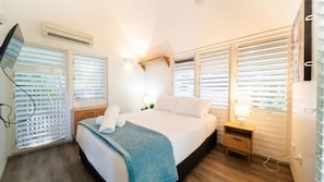 A hotel room with a bed, bedside table, lamp, and window blinds. - Palm Grove Cottage and Private Studio (South Townsville)