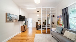 A modern living room with a sofa, TV, wooden floor, and a dining area with chairs and a table. - Palm Grove Cottage and Private Studio (South Townsville)