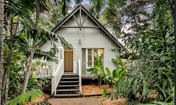A small, single-story building with a gabled roof, surrounded by dense tropical foliage. - Palm Grove Cottage and Private Studio (South Townsville)