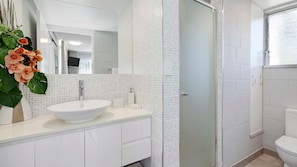 Un baño con lavamanos blanco, espejo y paredes con azulejos.