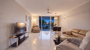 A modern living room with a flat-screen TV, leather sofa, and a dining area with a glass table.