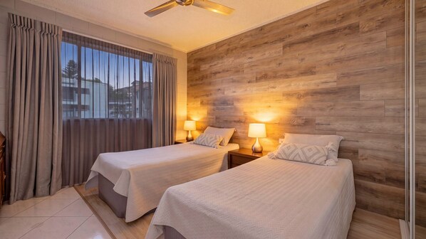 A hotel room with two beds, wooden paneling on the walls, and a view of the outside.