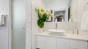 A modern bathroom with a white sink, a large mirror, and a vase of flowers. - Strand Oceanview Retreat (North Ward)
