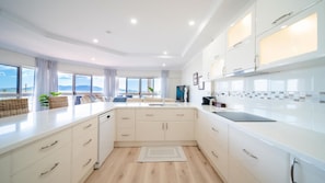 A modern kitchen with white cabinetry, a central island, and a view of the sea through large windows.