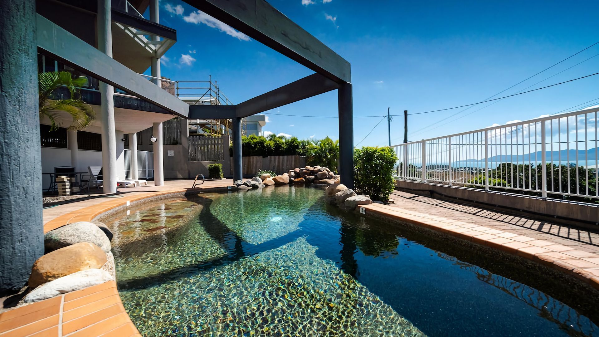 A swimming pool with clear water, surrounded by rocks and a small garden area.