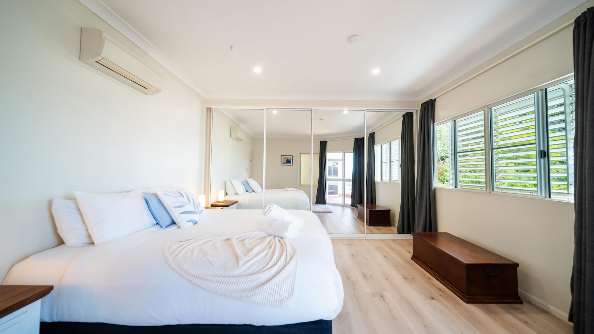 A hotel room with a large bed, a bedside table, a mirror, and a window with curtains.