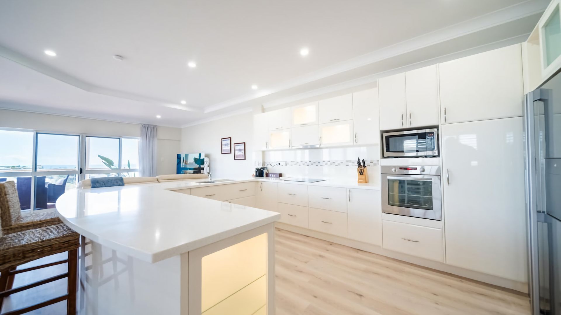 Uma cozinha moderna com armários brancos, uma ilha central e vista para o exterior.