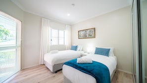 A hotel room with two beds, a window with blinds, a painting on the wall, and a wooden floor.