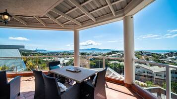 An outdoor patio with a table and chairs, overlooking a coastal landscape with buildings and mountains.