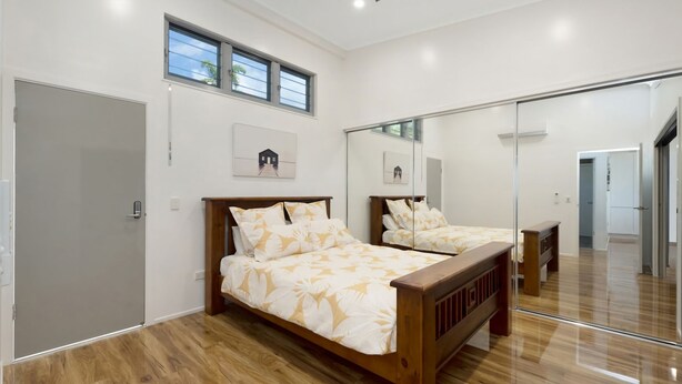 A bedroom with a wooden bed, a large mirror, and a door. - Searenity on Castle hill (Castle Hill)
