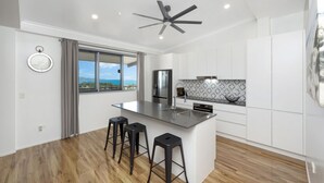 A modern kitchen with a central island, bar stools, a built-in oven, and a view of the sea. - Searenity on Castle hill (Castle Hill)