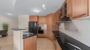 A modern kitchen with wooden cabinets, a black refrigerator, a stove, and a microwave. - Seaside Stays North Ward (North Ward)