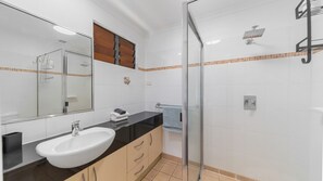Ein modernes Badezimmer mit einer Duschkabine aus Glas, einem weißen Waschbecken und einer schwarzen Arbeitsplatte.