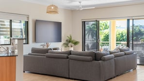 Een moderne woonkamer met een modulaire bank, een flatscreen televisie, een plafondventilator en een schuifdeur naar een buitengebied.