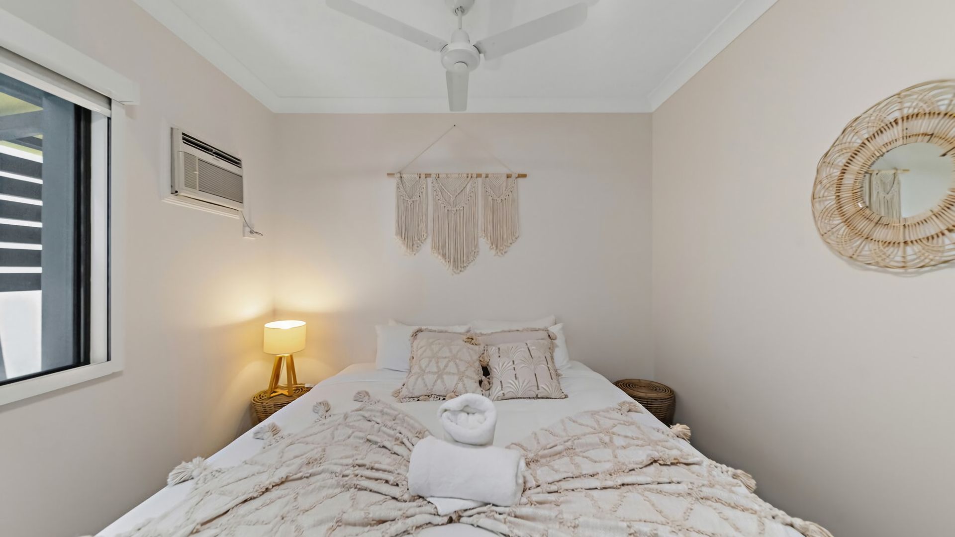 Ein Schlafzimmer mit einem Bett, einer Nachttischlampe, einem Deckenventilator, einer Wanddekoration aus Makramee und einer gewebten Wandverzierungen.