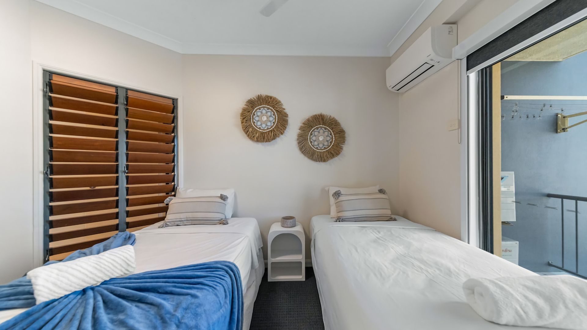 Ein Hotelzimmer mit zwei Betten, einem Fenster mit Jalousien, einer Klimaanlage und Wanddekoration.