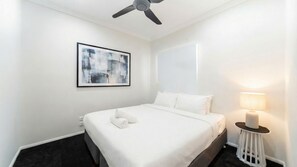 Ett hotellrum med en säng, en takfläkt, en abstrakt tavla som hänger på väggen och en sänglampa.
