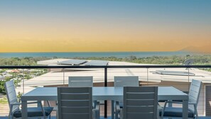 A dining area with a table and chairs, a view of a solar panel roof, and a distant landscape. - Executive Coastal Living with Ocean Views (Bushland Beach)